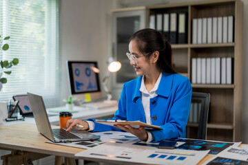 woman is sitting at a desk with a laptop and a clipboard