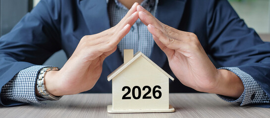 Businessman hands over wooden House model with 2026 New Year text. Property insurance and real...
