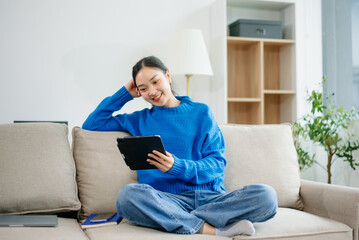 Young Asian woman relaxing on couch at home using smartphone and tablet. Joyful online shopping, digital lifestyle
