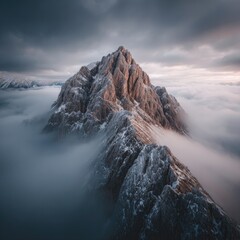 A majestic, snow-dusted mountain peak emerges from a sea of swirling clouds under a dramatic sky