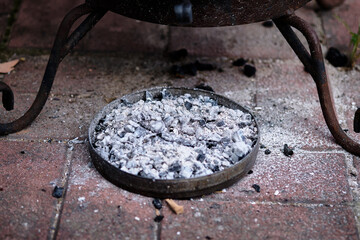 Ashes accumulate in a metal tray under a fire pit on a brick patio after a cozy evening gathering