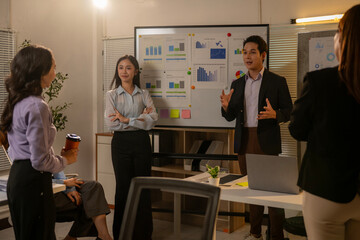 A group of people are standing around a white board with graphs on it
