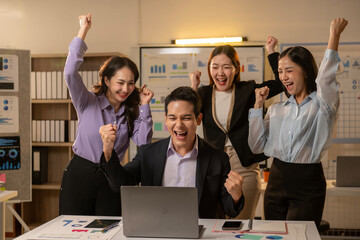 A man is sitting at a desk with a laptop and four women are standing behind him