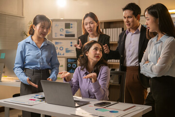 A group of people are standing around a table with a laptop