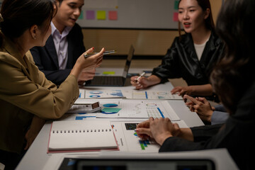 A group of people are sitting around a table with papers and laptops