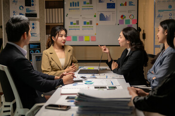 A group of people are sitting around a table with a white board behind them