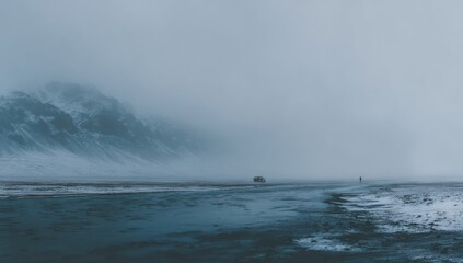 Naklejka premium Bleak landscape with a dark shoreline, distant figure, and a vehicle obscured by mist. Mountains shrouded in fog form the backdrop, evoking a sense of isolation and vastness