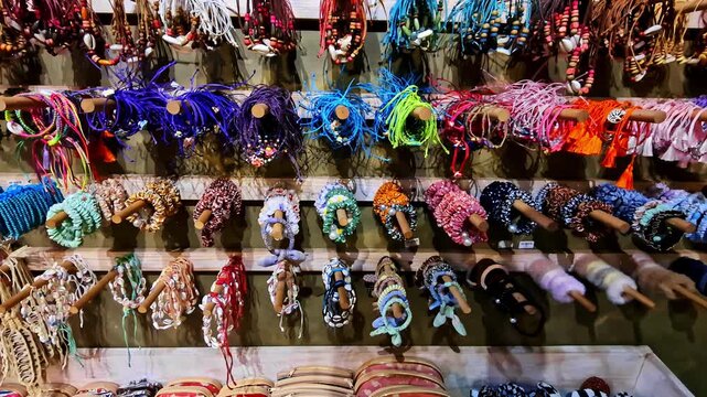 A vibrant collection of colorful, locally made woven bracelets, necklaces, and souvenirs hangs on a display wall at a traditional craft market stall in Ella, Sri Lanka.