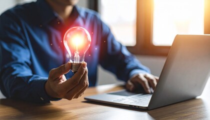 Man typing on laptop, holding lit lightbulb; bright, window background. Idea generation concept