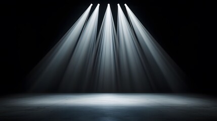 The image features a stark contrast, showing bright spotlights shining down onto a concrete floor in an otherwise dark and undefined space, creating a dramatic effect.