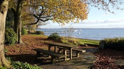 Obraz premium Autumnal park scene by a waterway with a picnic table. Sunlight streams through the trees