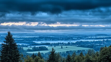Misty, panoramic landscape view of fields and forests beneath a dramatic sky