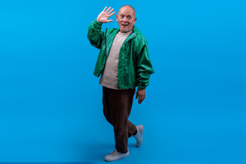 Mature Asian Man Walking While Waving Hello With Smile Isolated On Blue Background