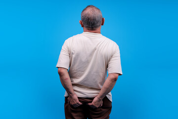 Back View Of Elderly Asian Male Feeling Pain And Discomfort On His Buttocks Against Blue Background