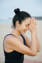Yoga instructor meditating on the beach with hands together and eyes closed