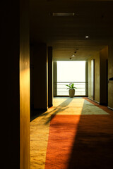Morning sunlight streaming into a hotel corridor through the window at the far end, casting warm golden tones on the walls and carpet, creating a serene and inviting atmosphere.