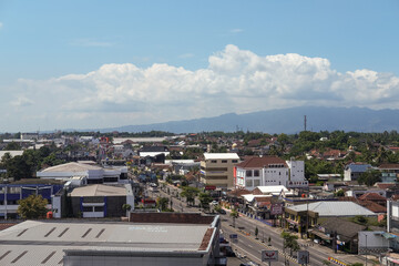 Magelang cityscape stretches under a bright blue sky, with rows of rooftops, busy streets, and...