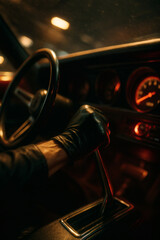 Gloved hand shifts gears in dimly lit vintage car interior, illuminated by red gauge lights, capturing a sense of mystery and action.