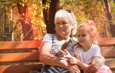 Loving granddaughter hugging her grandmother, engaged in conversation, creating warm, familial atmosphere, walking together in summer park. Happy family. Having good times with grandparent outdoors.