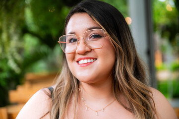 Young Woman Smiling at Outdoor Café Table with Natural Green Background