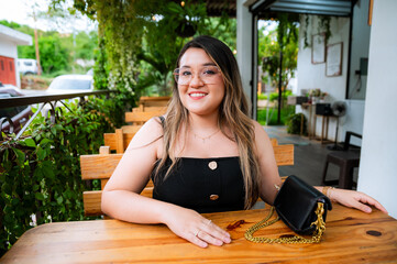 Young Woman Smiling at Outdoor Café Table with Natural Green Background