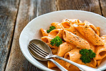 Creamy tomato and stracciatella pennone rigato noodles on wooden table