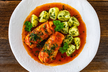 Stuffed cabbages with tomato sauce and boiled potatoes on wooden table - polish cuisine golabki