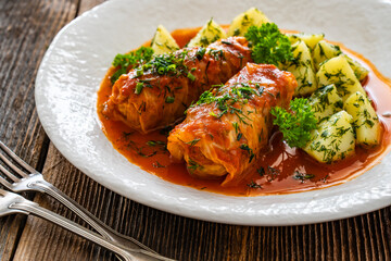 Stuffed cabbages with tomato sauce and boiled potatoes on wooden table - polish cuisine golabki