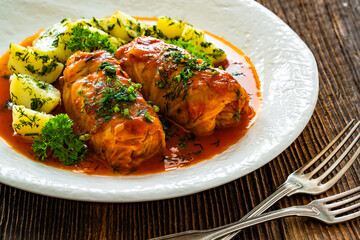 Stuffed cabbages with tomato sauce and boiled potatoes on wooden table - polish cuisine golabki