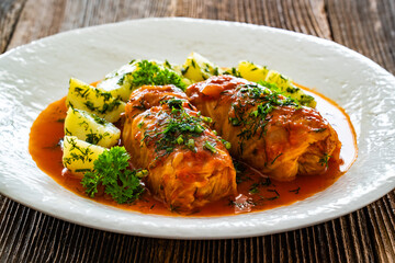 Stuffed cabbages with tomato sauce and boiled potatoes on wooden table - polish cuisine golabki