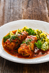 Stuffed cabbages with tomato sauce and boiled potatoes on wooden table - polish cuisine golabki