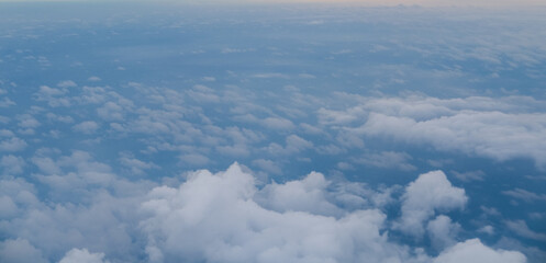 Expansive aerial view of soft white clouds scattered over a deep blue sky, creating a tranquil and airy atmosphere with gentle light highlighting the texture of each cloud.