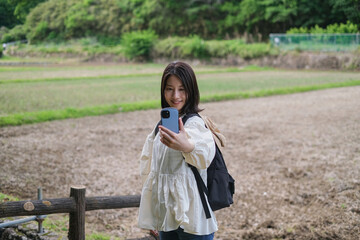 畑を背景にスマートフォンで自撮りする女性