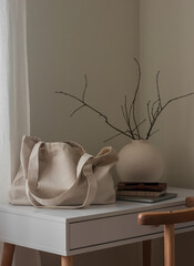A shopping bag, a notebook, a vase with branches on a white table in the living room. Cozy minimalistic interior