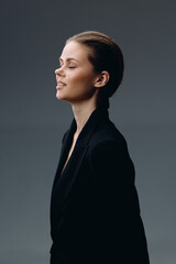 Profile of peaceful woman with closed eyes wearing black jacket in soft light against dark...