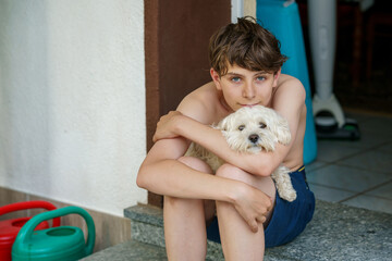 Teenage boy hugging his young Maltese family dog. Real life, real people moment of friendship, love, and bonding between pet and owner. Warm, emotional connection at home.
