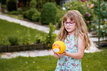 Little elementary school girl playing with a ball in home garden on a sunny summer day. Real life, real people, active outdoor childhood fun in domestic backyard.
