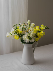 A simple garden bouquet in a white enameled jug on a table with a white muslin tablecloth