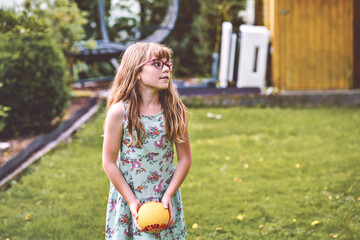Little elementary school girl playing with a ball in home garden on a sunny summer day. Real life, real people, active outdoor childhood fun in domestic backyard.