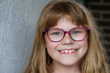 Portrait of cute, happy, smiling elementary school girl with eyeglasses and long blond hair. Real life, real people, natural childhood joy and confidence in everyday setting