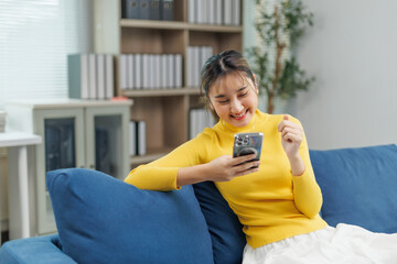 Happy asian freelancer working remotely from home office sitting on comfortable sofa, using mobile...