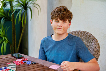 Portrait of smiling teenage boy playing poker with friends, holding chips. Real life, real people, fun game night, youth lifestyle, strategy and friendship
