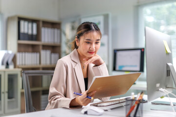 Young professional woman reviewing paperwork and working on a computer, maintaining focus in a...