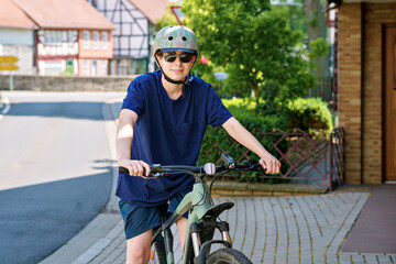 Teenager boy wearing helmet and sunglasses riding a bicycle in the city. Active lifestyle, urban youth, safety gear, outdoor fun, and healthy transportation