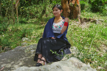 Indigenous woman wearing traditional clothes sitting on a rock in the forest