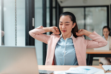 Asian office worker is relaxing her muscles after working on computer for a long time, she is stretching her arms and back to relieve stress and pain