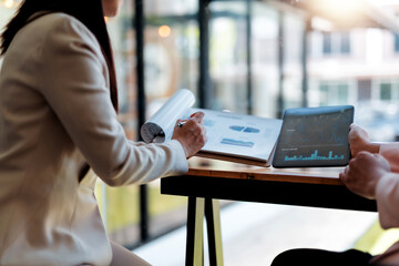 Two businesswomen discussing financial charts and graphs on a tablet and printed reports,...