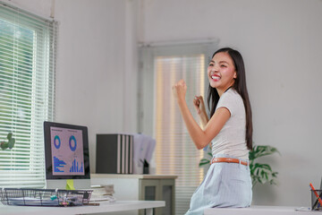 Young Asian office worker is celebrating a great achievement looking at positive sales data on her...