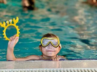 Happy little girl with in swimming pool learning to dive. Little school child with swimm glasses, picking things from pool bottom. Healthy sport activity and fun for children.