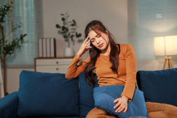 Stressed young woman having headache and touching her temples while sitting on sofa in living room...